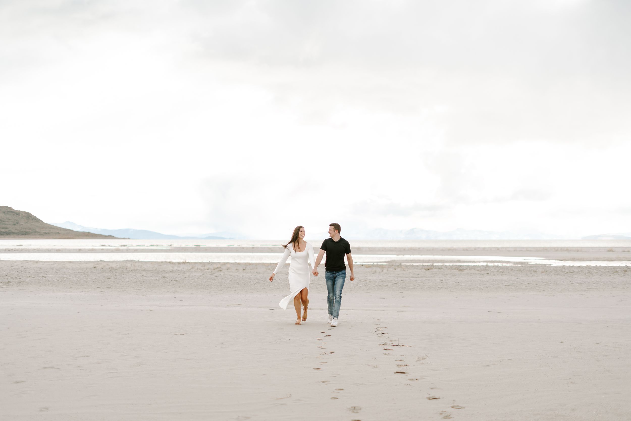 Couple walking together leaving footprints in the sand on an overcast beach.