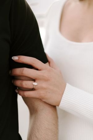 Close-up photograph of hands showing an engagement ring against black and white clothing.