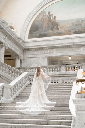 A flowing white wedding dress with a long veil captured on an elegant marble staircase with classical architecture.