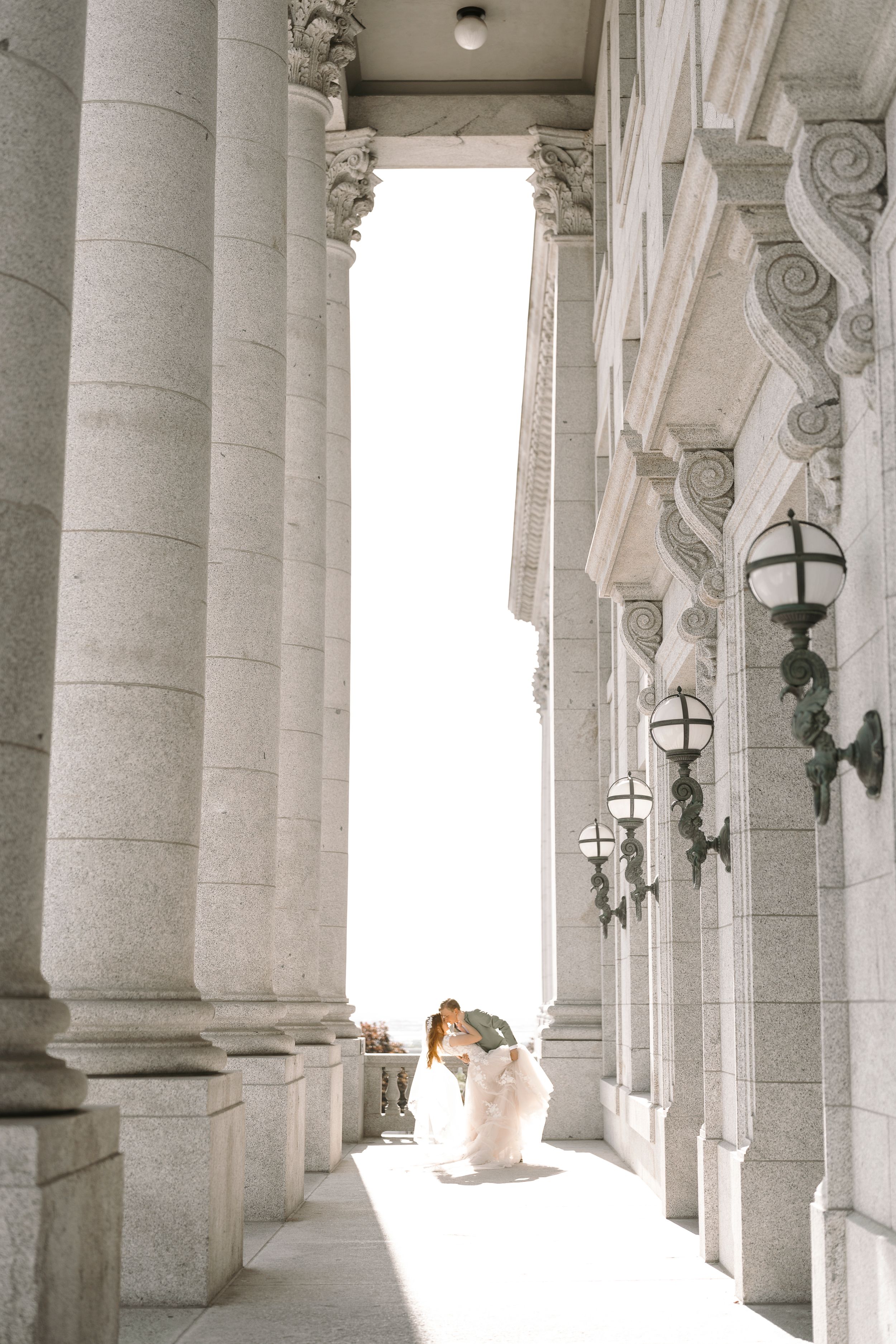 A columned marble hallway with classical architecture and sunlight streaming through the windows.