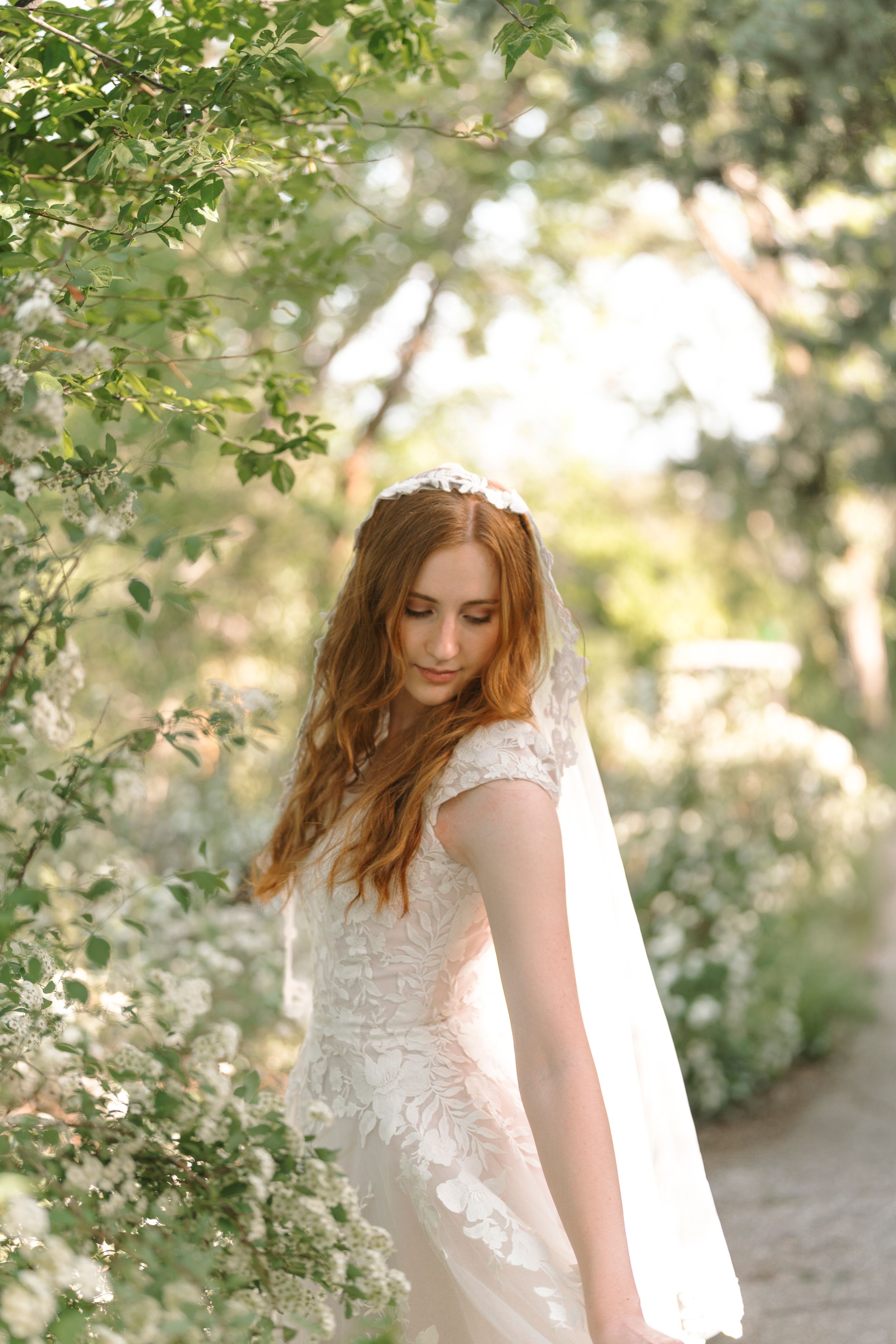 Ethereal garden bridal portraits showing a flowing white lace dress among sunlit green foliage.