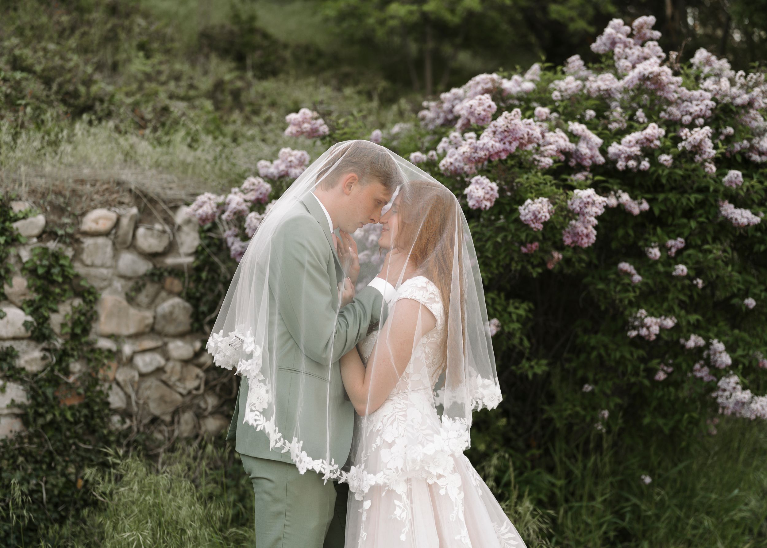 A romantic garden wedding moment with a couple nestled among pink flowering bushes.