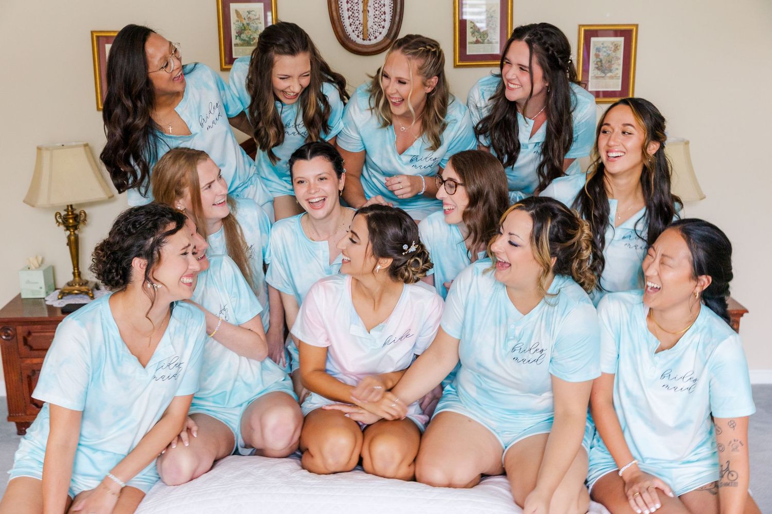 Friends in matching blue shirts sharing laughs while sitting together on a bed.