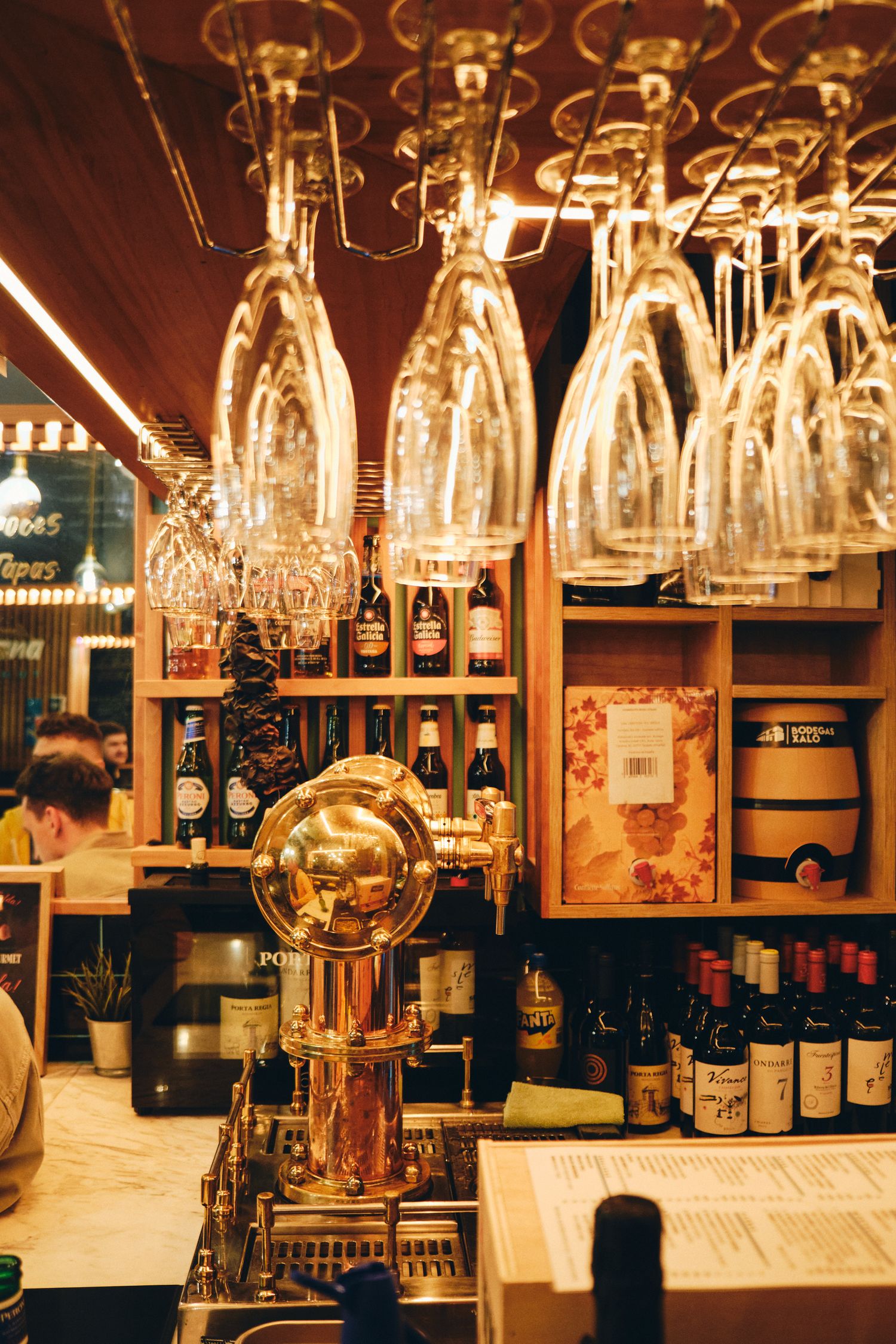 Bar interior with hanging wine glasses and beer taps in warm amber lighting.