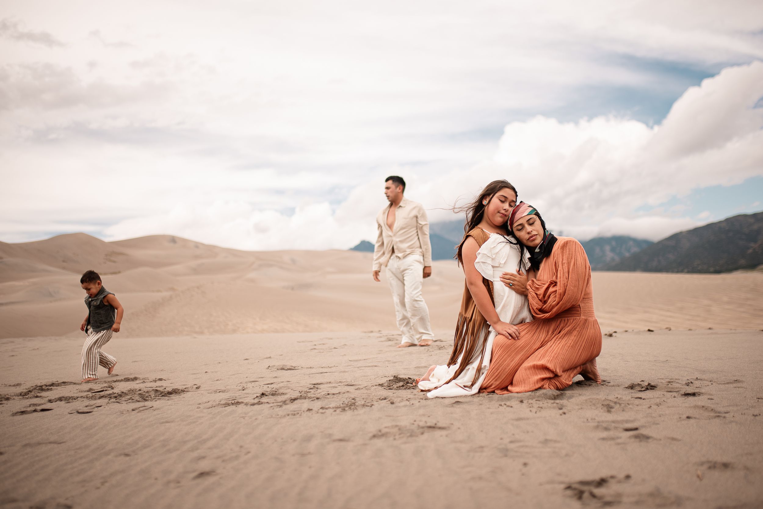 Mother embraces daughter while father chases toddler in the back at the Great Sand Dunes, Colorado.