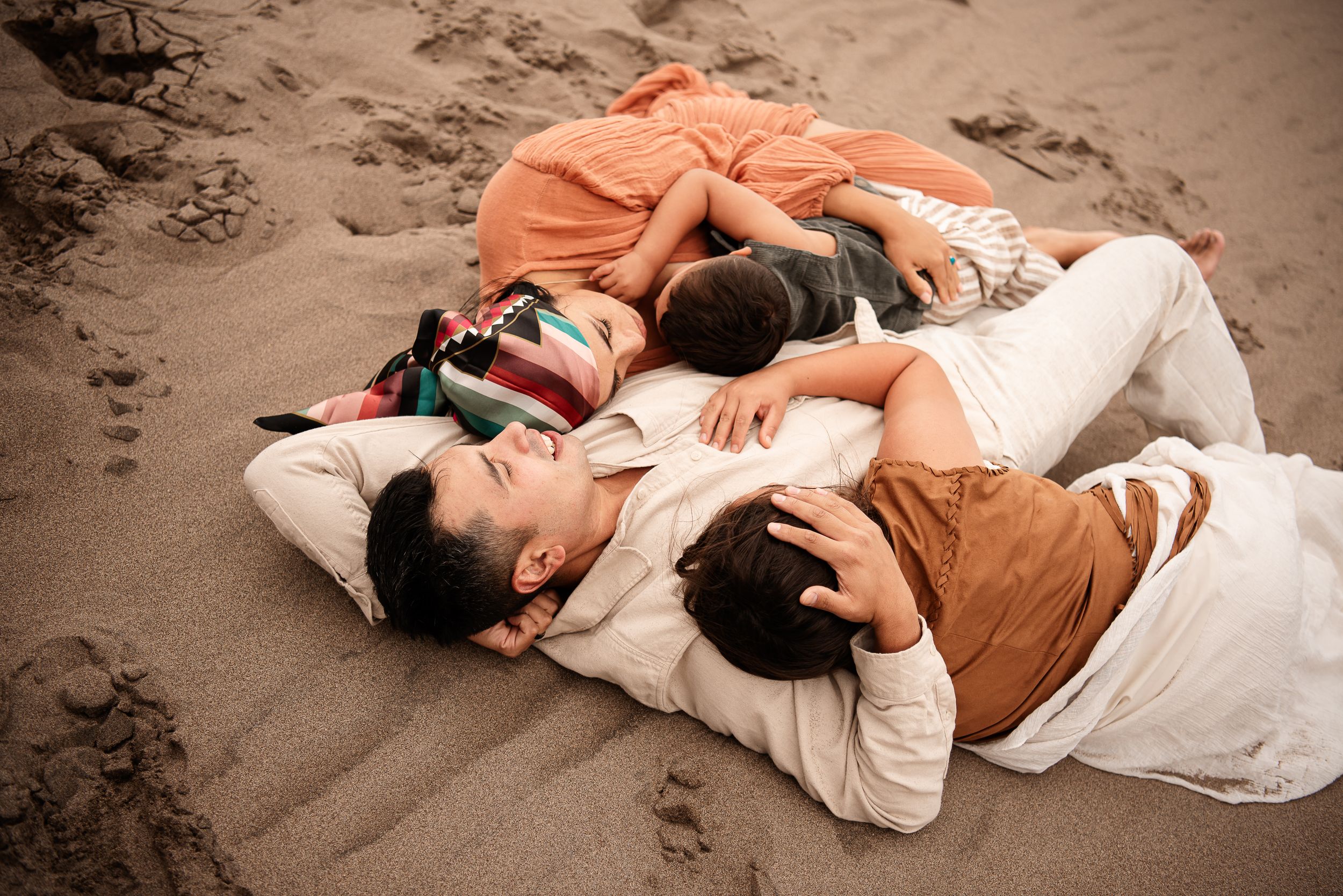 family embracing on the sand laying down at the Great Sand Dunes Colorado