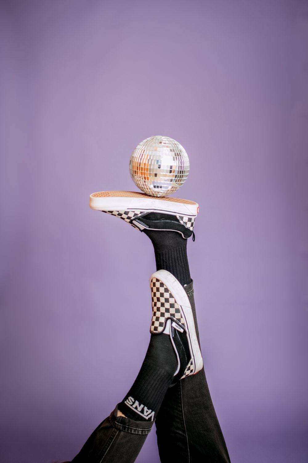 A disco ball balanced on a checkered Vans sneaker against a purple background.