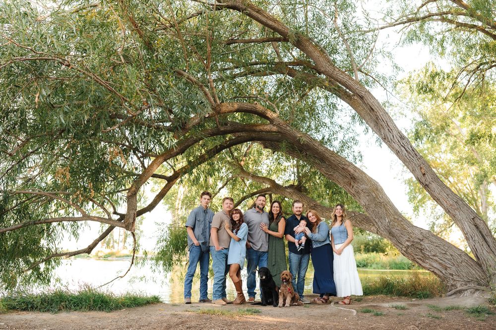 A group photo session under a large willow tree in a natural outdoor setting.