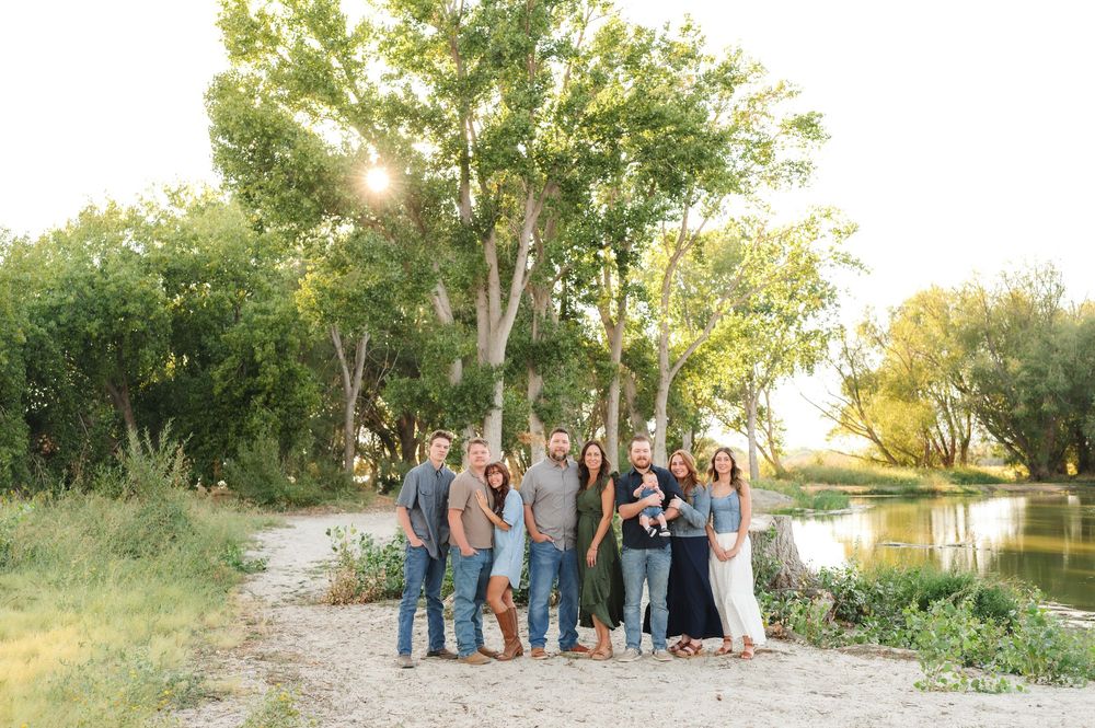 A group stands together on a gravel path near a pond with tall trees and golden sunlight filtering through the foliage.