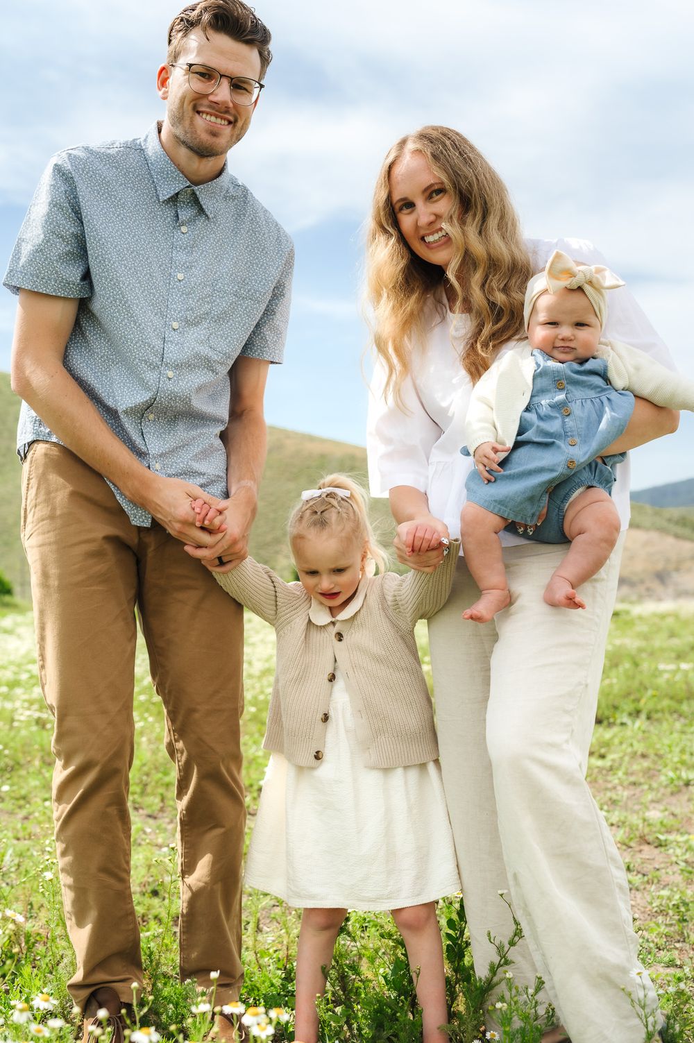 Casual family portrait in a field of white wildflowers with mountains visible in the distance.