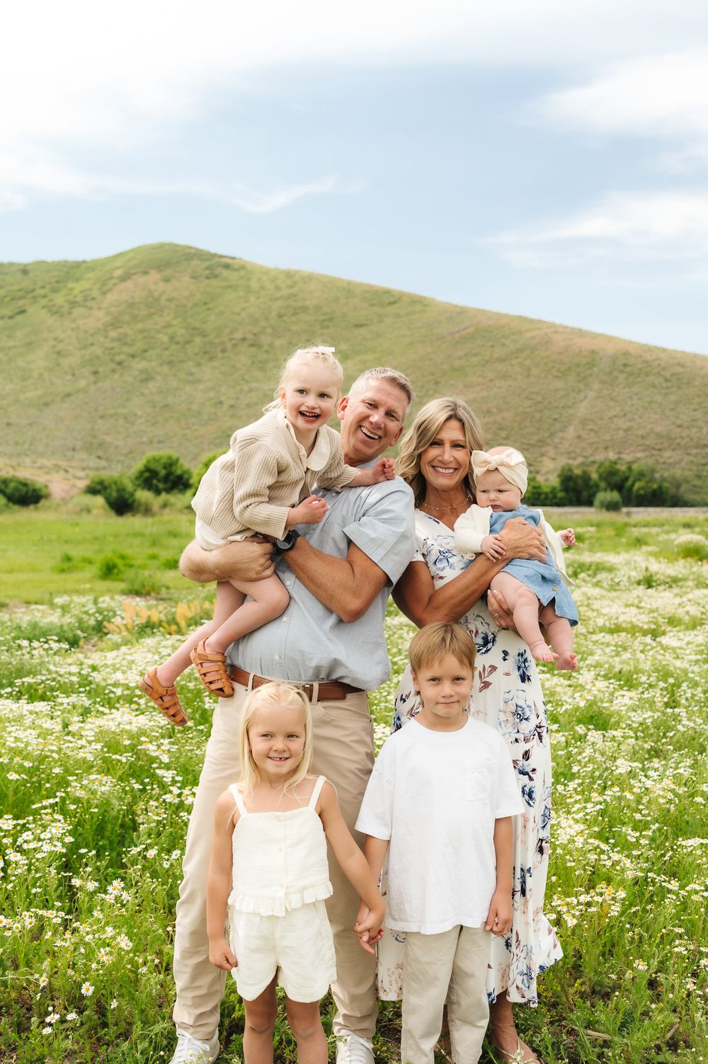 Happy family moment captured in a blooming meadow with rolling hills in the background.