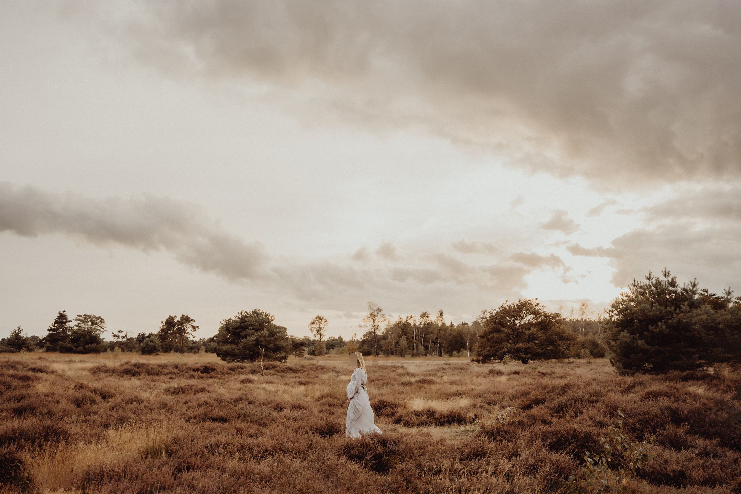 A white flowy dress stands out against a moody landscape with cloudy skies at sunset.