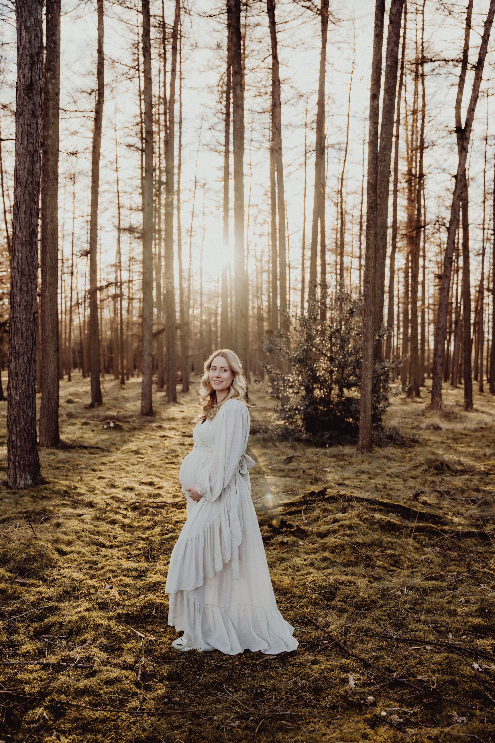 A flowing white dress contrasts against a sunlit pine forest background.