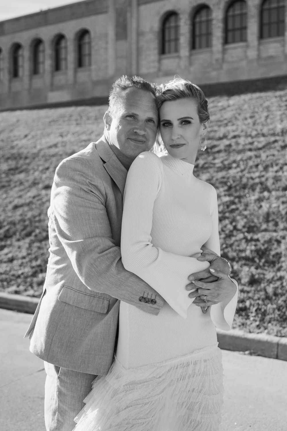 A romantic black and white photo series of a couple embracing outdoors on a hillside in formal attire.