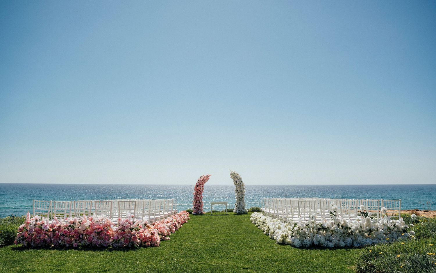 A beautiful beachside wedding ceremony setup with coral chairs and a white floral arch.