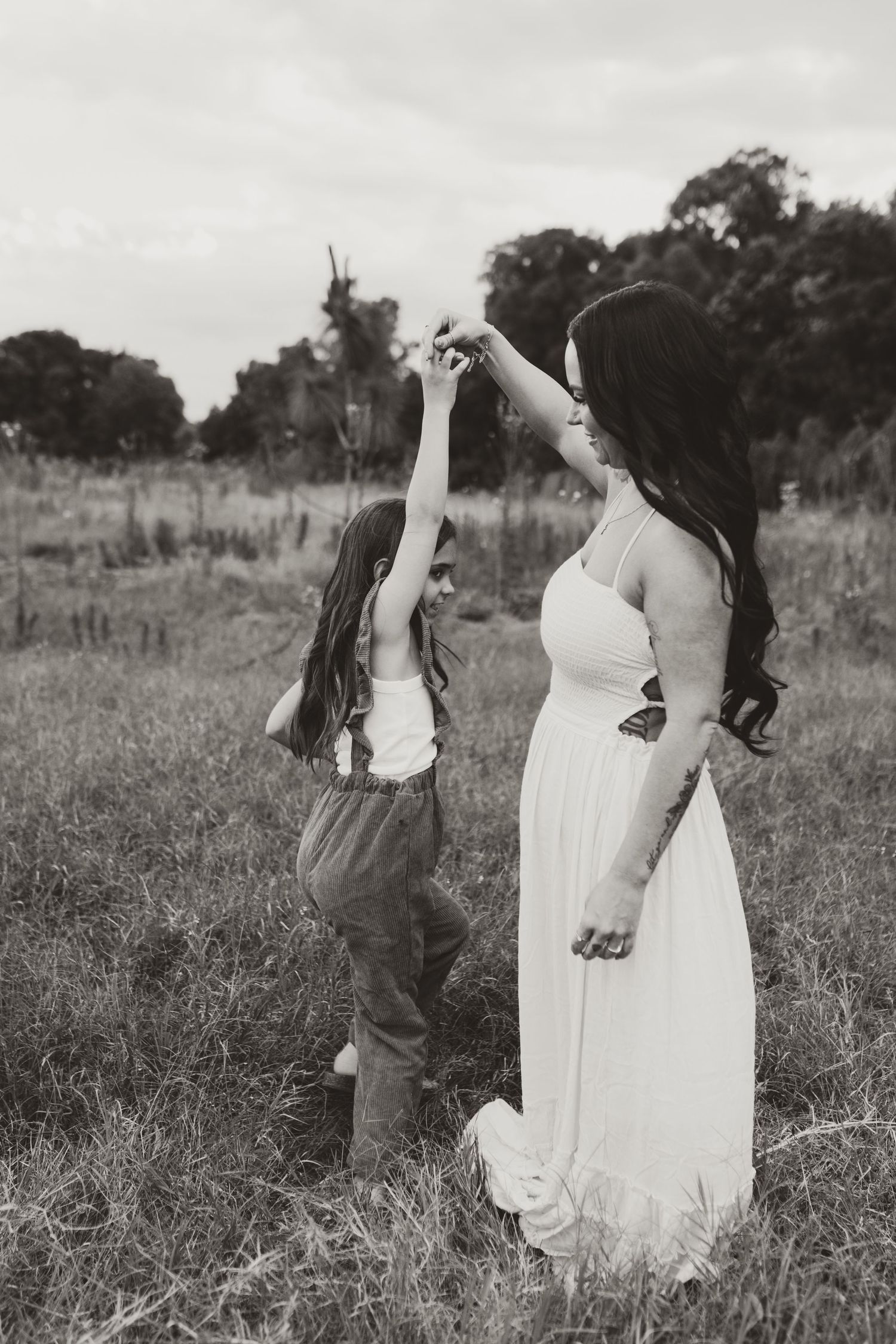 Black and white photo of two people in dresses dancing joyfully in a grassy field.