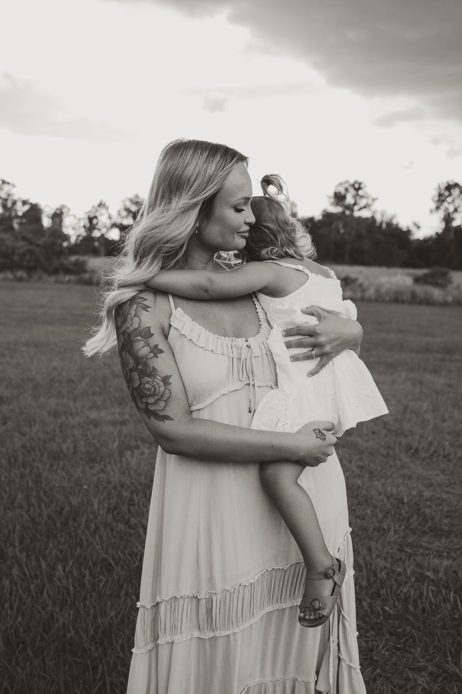 A touching black and white outdoor photograph showing an intimate moment between figures in white dresses in a field.