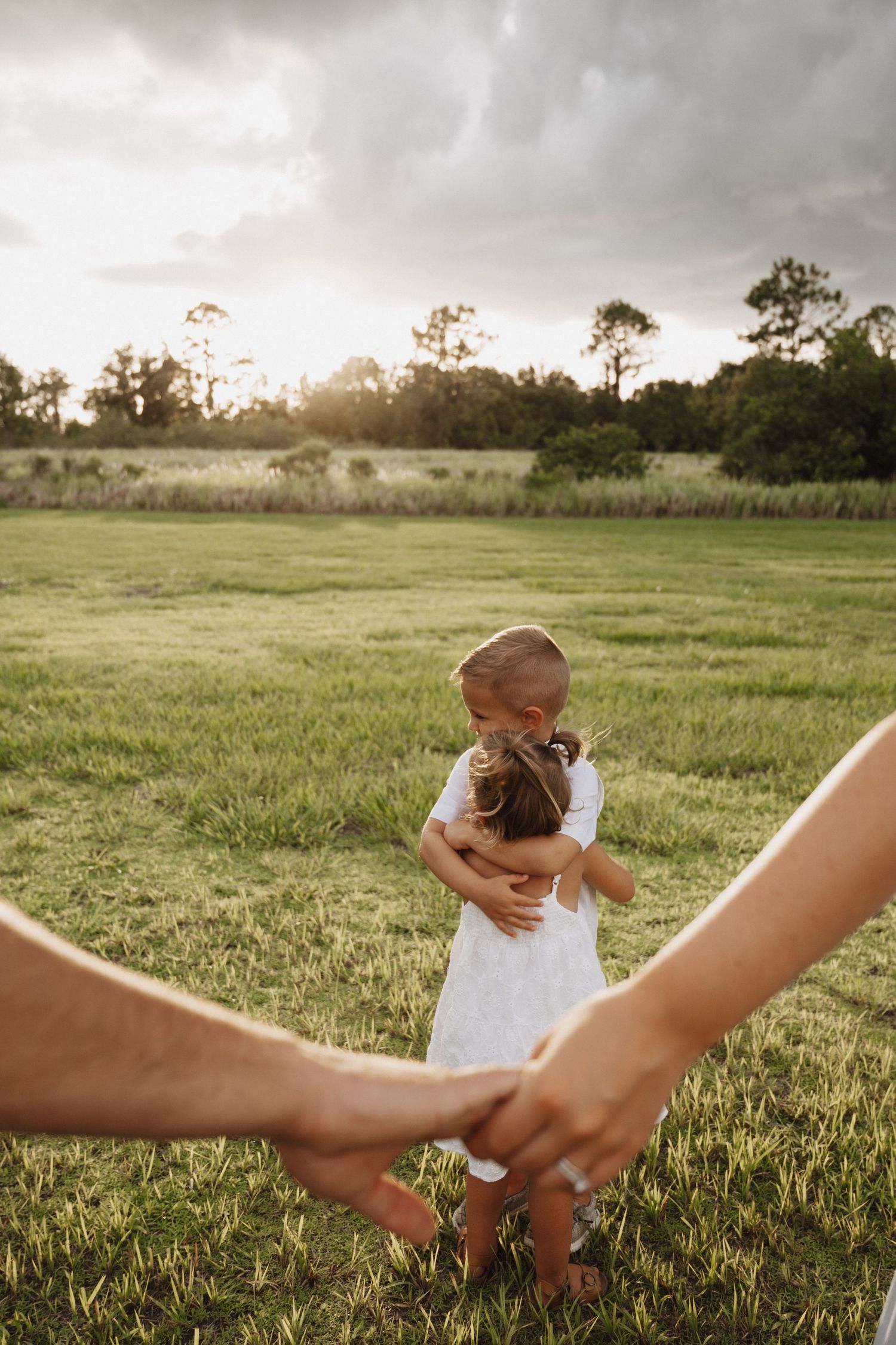 People holding hands in a golden field at sunset while walking together in a line outdoors.