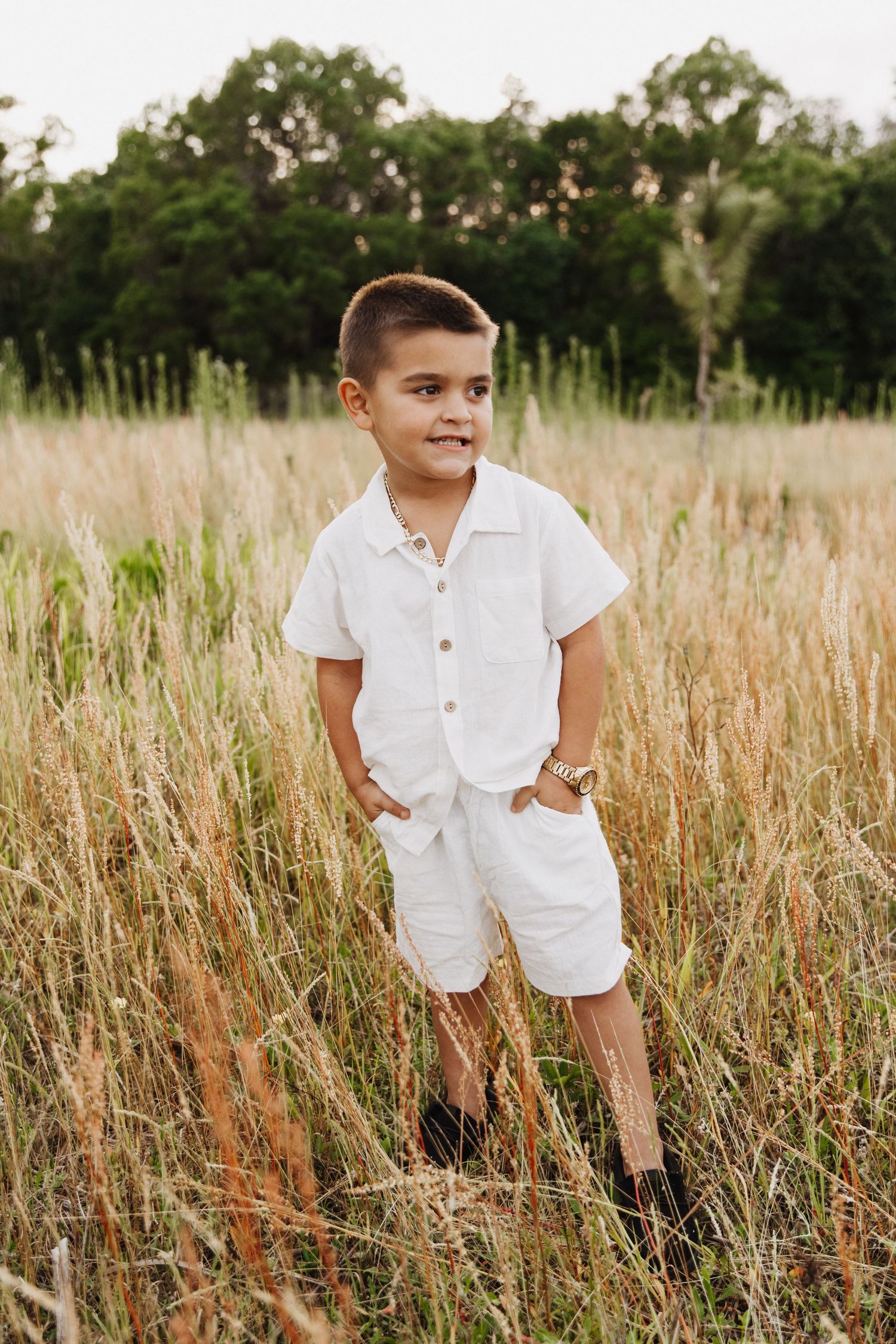 A child wearing an all-white summer outfit stands in a golden wheat field during sunset.