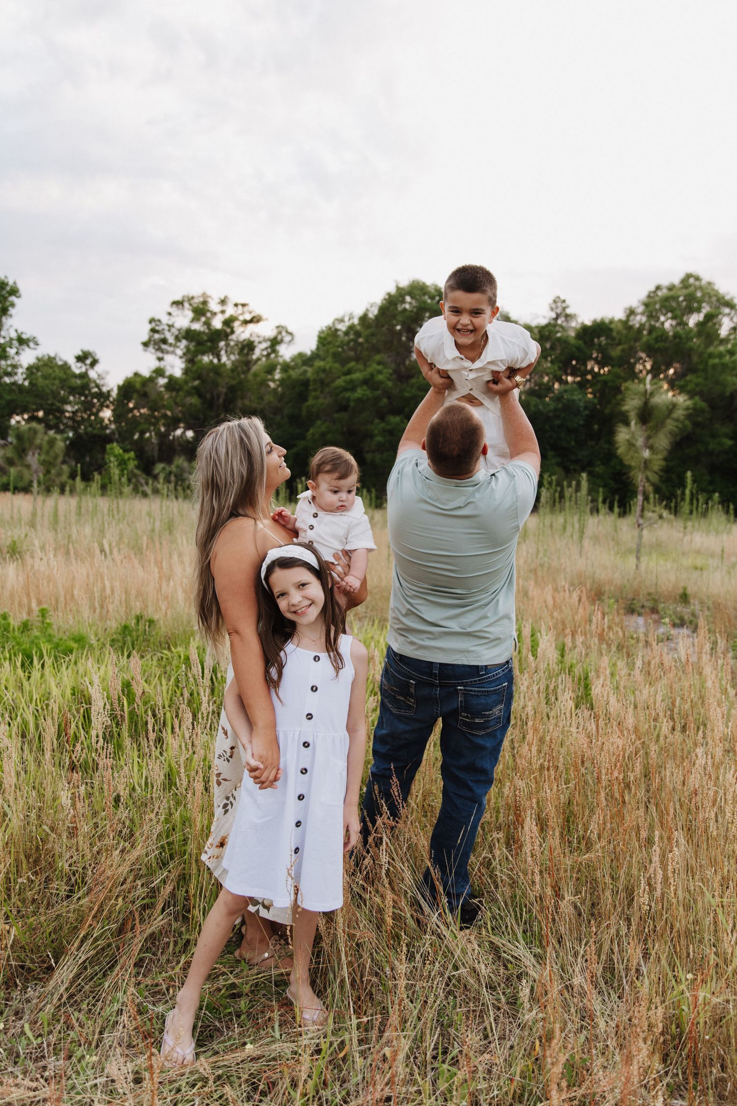 A family having fun together in a tall grass meadow during golden hour while wearing casual summer clothes.