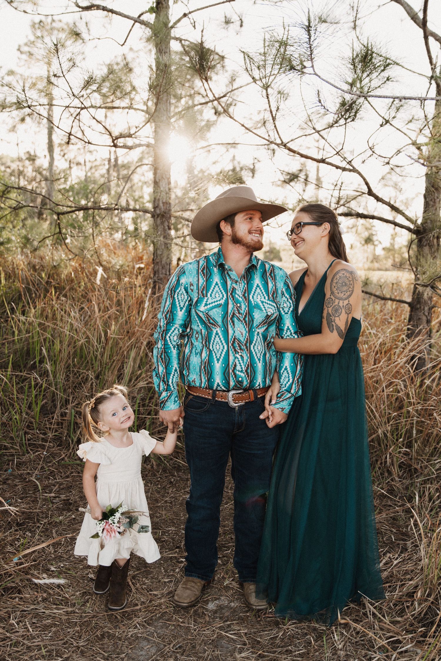 Romantic family photoshoot in a natural outdoor setting with tall grass and trees in muted earth tones.
