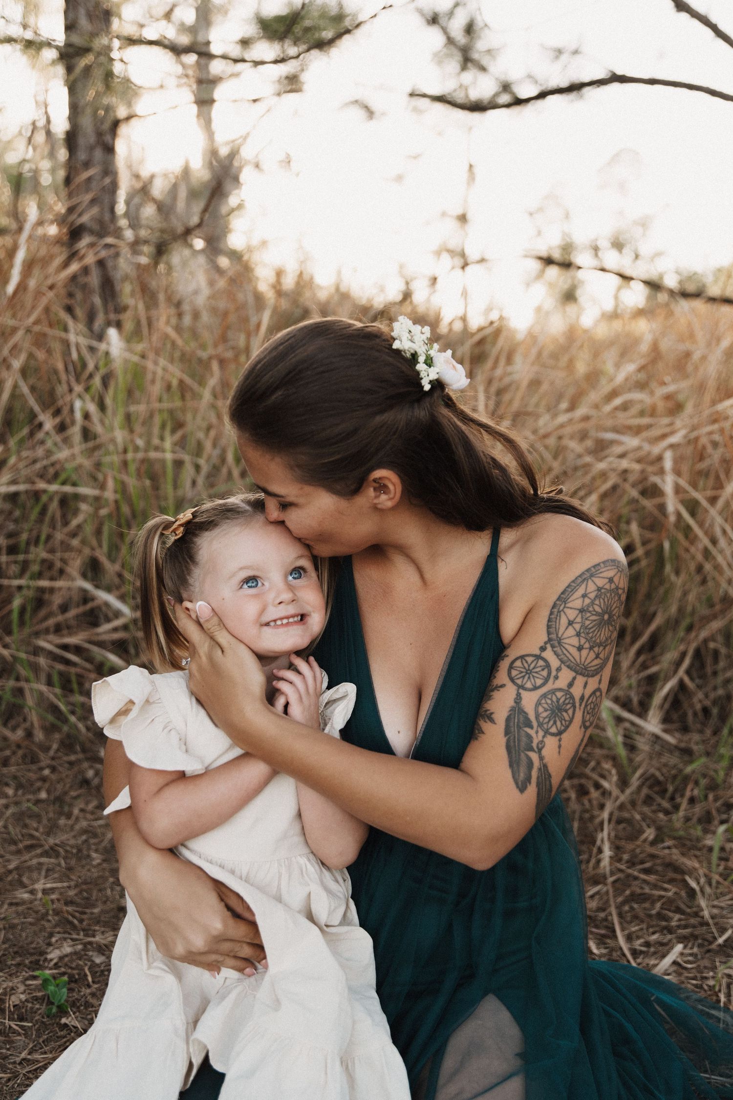 A tender moment captured between figures wearing white and teal dresses against a natural outdoor backdrop.