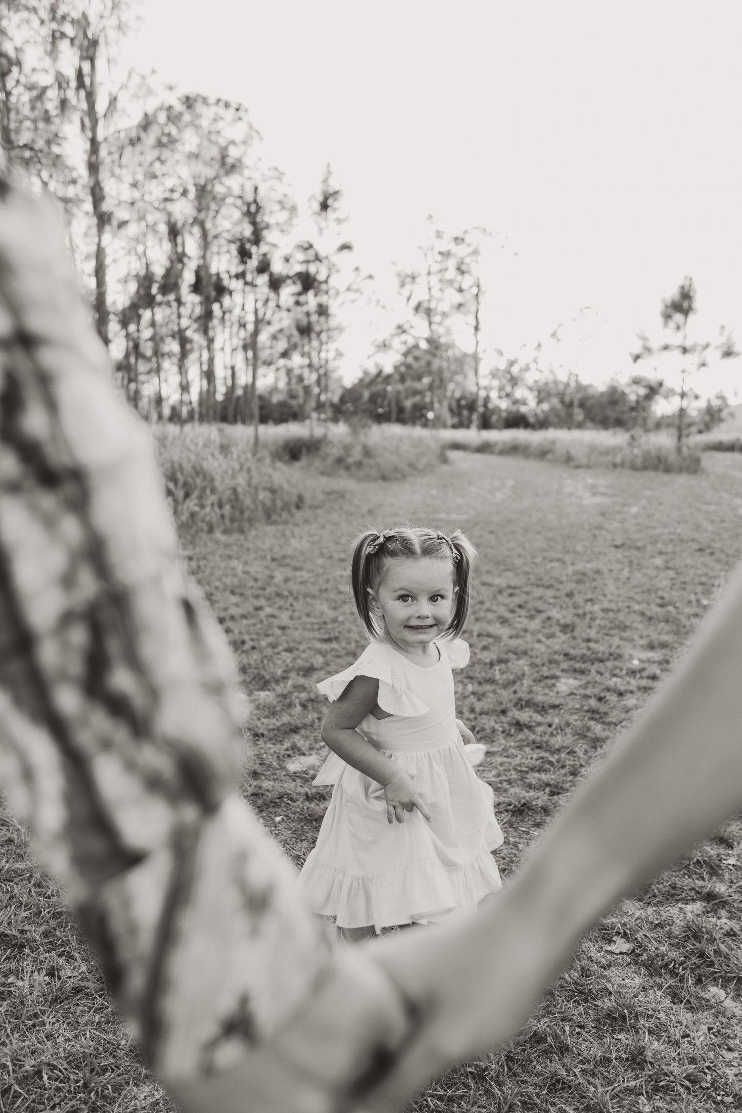 Four sequential black and white photos show a child in a light-colored dress sitting in a grassy field.