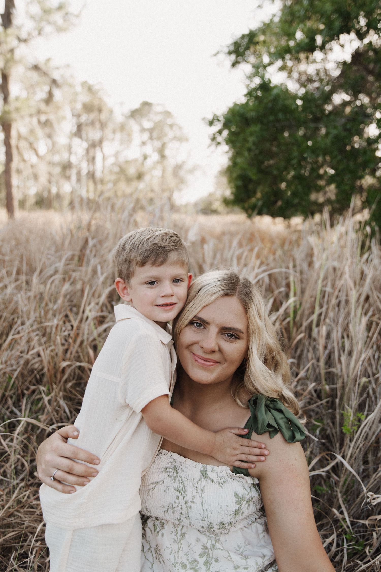 A loving embrace between parent and child captured in a sun-drenched field of tall wild grasses.