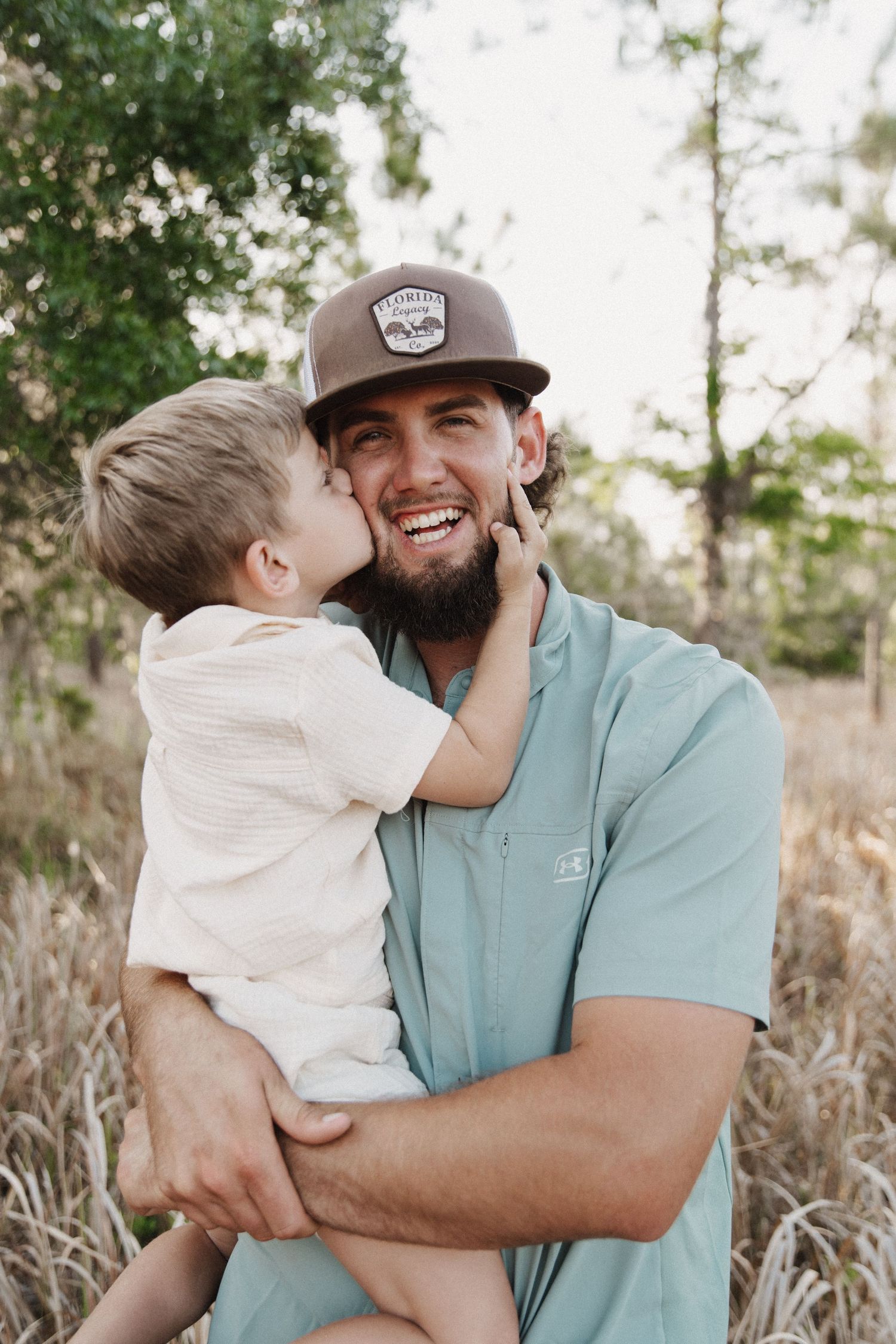 Sweet candid moment of embrace captured in natural lighting against tall grasses and trees in the background.