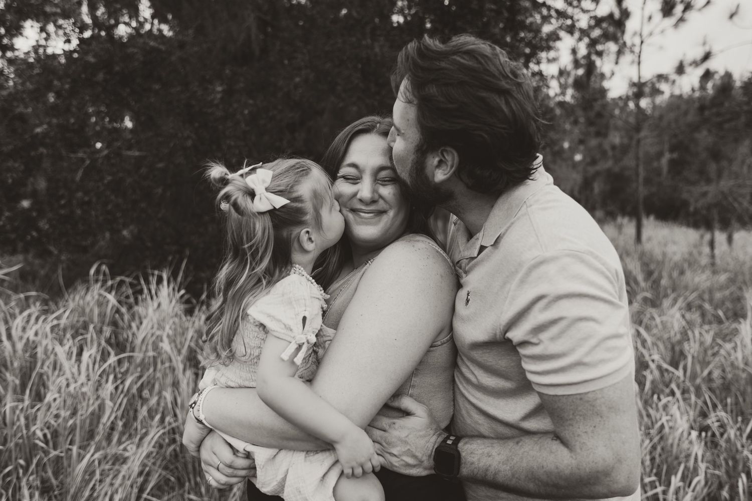 A series of black and white photographs showing affectionate moments and embraces in a grassy outdoor setting.