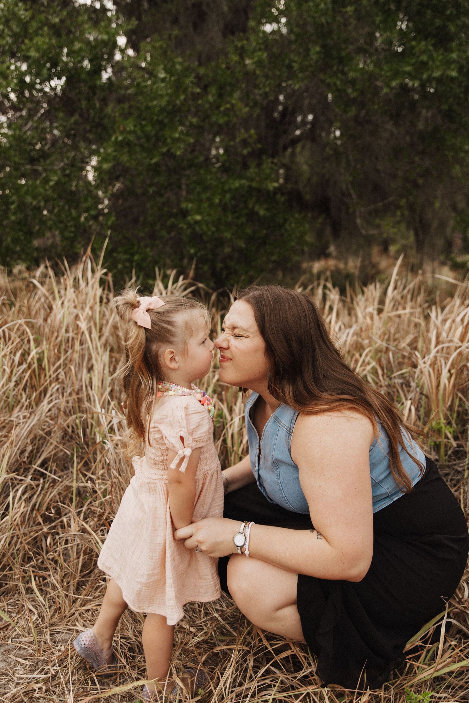 A tender moment shared between parent and child lying in a field of tall beige grass during golden hour.