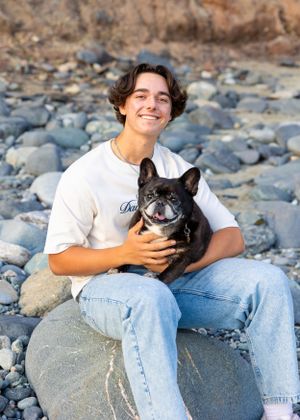 High school senior boy sitting on beach with his dog