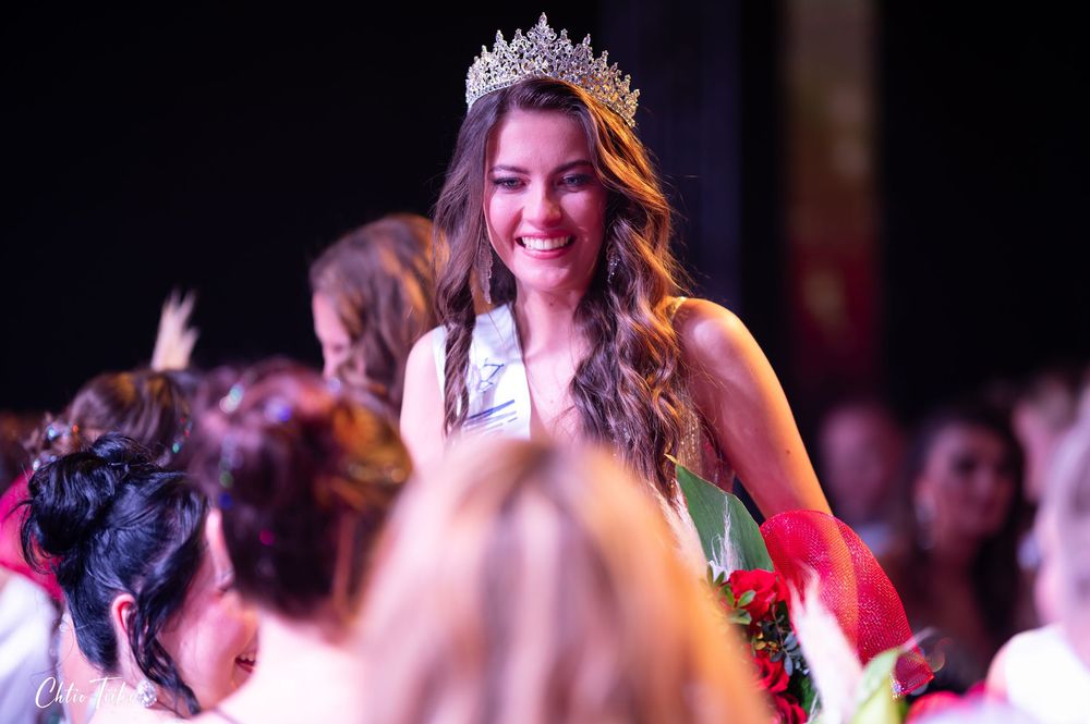 Smiling woman wearing tiara and sash crowned at beauty pageant.