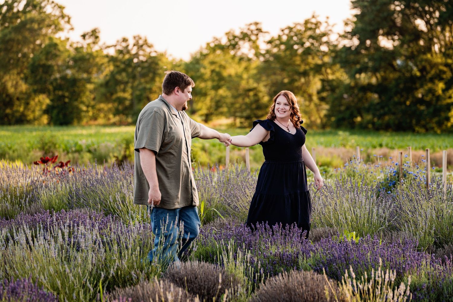 A romantic couple stands hand in hand amid a field of blooming lavender flowers at sunset.