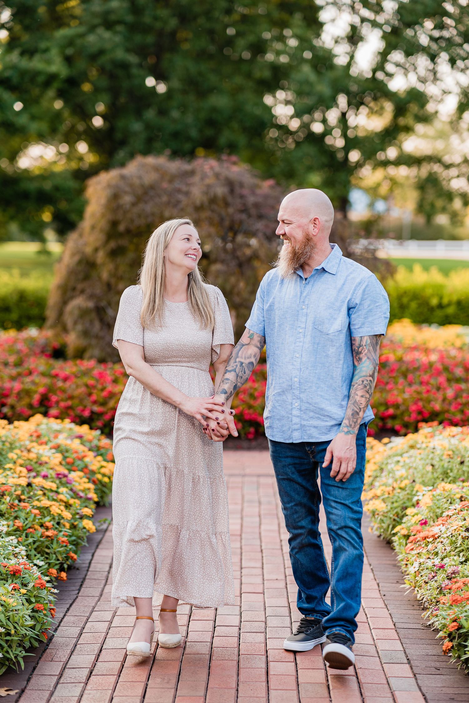 A couple walks along a garden path lined with vibrant rose bushes during a golden sunset photo session.