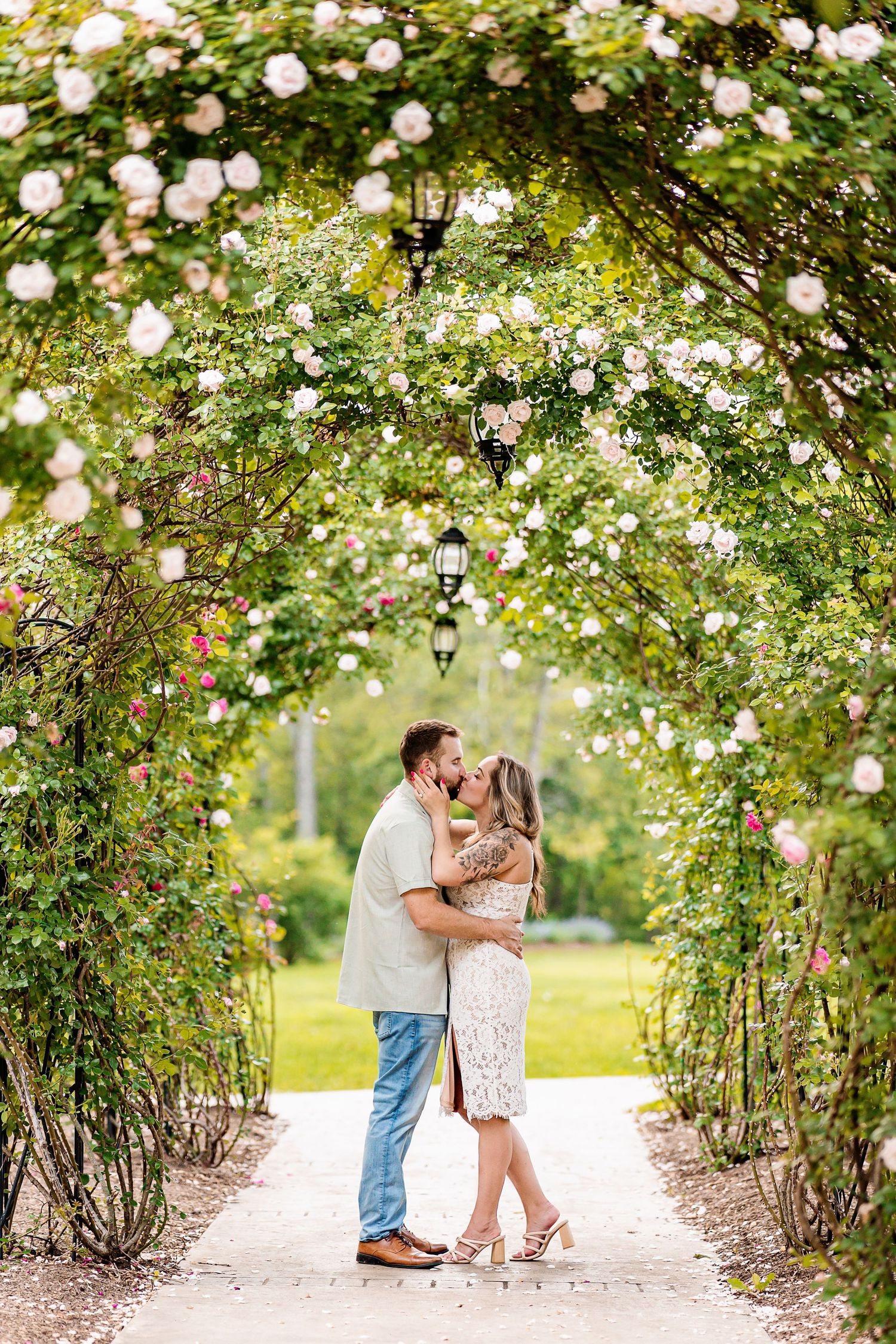 A romantic moment under a beautiful flowering archway with white roses and lanterns in a garden setting.
