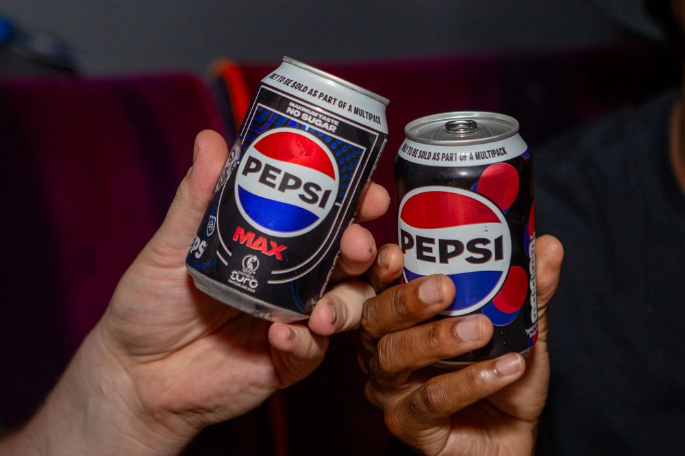 Hands holding Pepsi cans in dramatic lighting at a social gathering.