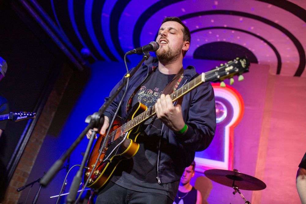 Musicians performing on stage with colorful purple and blue lighting effects.