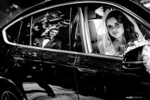 A black and white photograph shows a bride in white inside a car window at night.