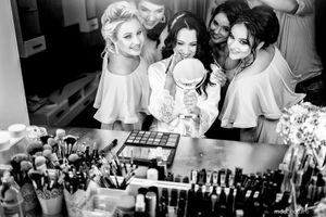 Black and white photo showing preparation at a makeup station with cosmetics and styling products arranged on table.