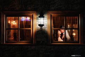 A romantic silhouette through illuminated windows at night with a vintage wall sconce between the frames.