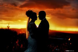 Silhouetted couple embraces against a dramatic orange and gold sunset sky, creating a romantic wedding portrait.