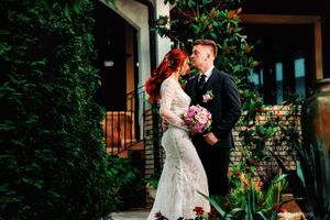 A newlywed couple embraces in front of a garden entrance with lush greenery and flowers.