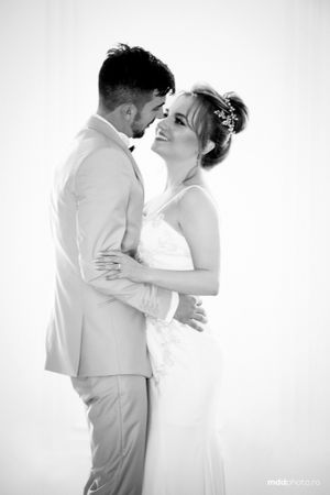 A romantic black and white wedding photo showing a loving couple embracing in matching light attire against a bright background.