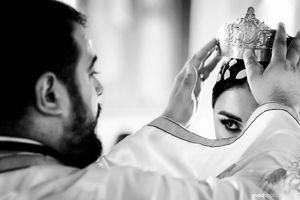 A black and white photograph showing hands holding up a crown in a reflective ceremonial moment.