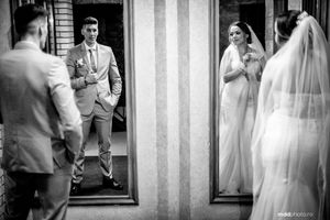 Black and white reflection photograph showing wedding preparations with mirrored views through doorways.