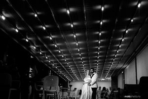 A person in a white dress stands beneath a dramatic geometric ceiling with recessed lighting in a large empty room.