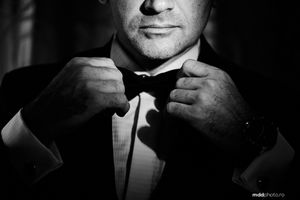 Black and white close-up shot of hands adjusting a bow tie on formal evening wear.