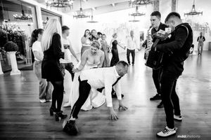 People interact and dance during a casual gathering on a polished wooden floor in a bright indoor space.