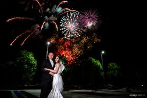 A couple shares a romantic moment at night while colorful fireworks explode in the sky above them.